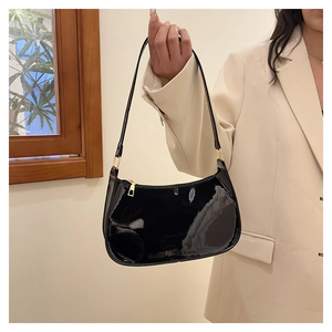 Detail of glossy black patent leather baguette bag with premium gold metal zipper and buckle