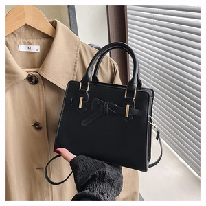 Close-up of black leather handbag with gold metal buckles and stylish knot strap detail