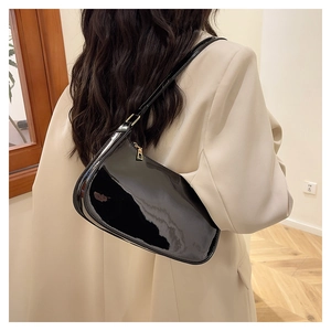 Close-up of black patent leather baguette bag with gold metal zipper and slim shoulder strap