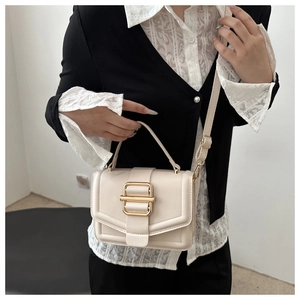 Close-up of creamy white crossbody bag with gold metal buckle and top handle detail
