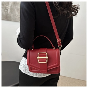 Side view of red leather crossbody bag with gold buckle on a model wearing black knitwear