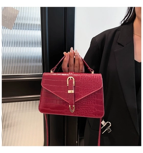 Detail of red crocodile textured handbag with golden metal clasp and flap design