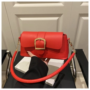 Macro shot of red leather handbag featuring a bold golden horseshoe buckle and strap detail