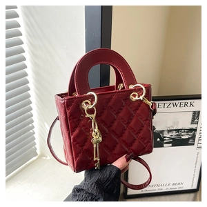 Detail of burgundy quilted leather bag with gold ring handle and unique key charm
