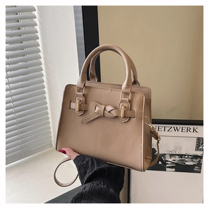 Close-up of beige handbag featuring decorative bow design and gold-tone hardware detail