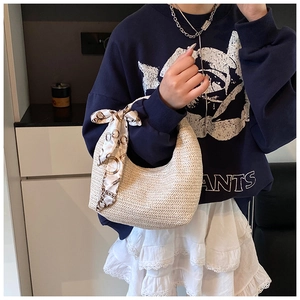 Détail d'un sac demi-lune tressé beige avec un foulard décoratif en soie à motif chaîne