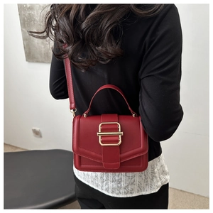 Détail du petit sac carré rouge avec boucle magnétique dorée porté à l'épaule