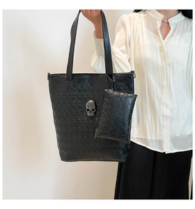 Detail of black leather tote bag with embossed skull patterns and metal skull logo