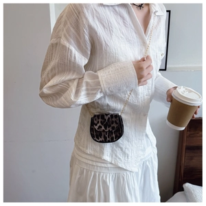 Mini leopard print saddle bag featuring a gold chain strap on a stylish white outfit