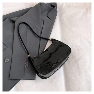Flat lay of black glossy hobo bag on white cloth with grey suit jacket background
