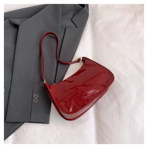 Close-up of a glossy red patent leather underarm bag featuring a gold buckle detail