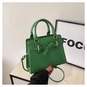 Detail of green satchel featuring leather bow, gold hardware, and adjustable strap