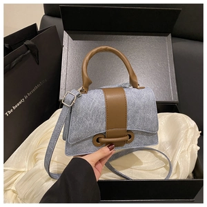 Detail of denim hourglass handbag with brown leather trim in a premium black gift box