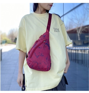 Detail of red tie-dye nylon sling bag showing zipper pocket and waterproof texture