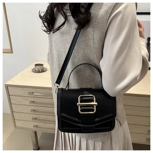 Detail of black crossbody bag featuring elegant gold metal buckle and leather texture
