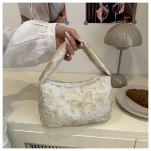 Detail of embroidered butterfly pattern on a cream fabric shoulder bag with zipper