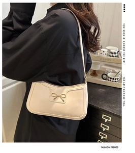 Close-up of cream leather underarm bag featuring a golden metallic bow detail