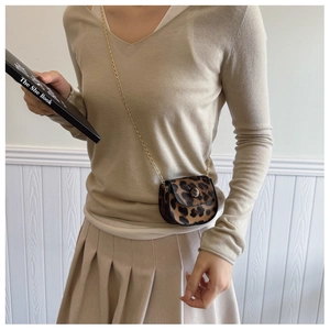 Close-up of leopard print mini crossbody bag with gold chain strap on a beige outfit