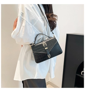Detail of black crocodile texture shoulder bag with gold hardware worn by a model