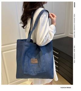 Detail of dark blue denim tote bag featuring large front pocket and brown leather logo patch