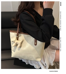 Detail of off-white tote bag featuring brown contrast handles and a cute dog charm