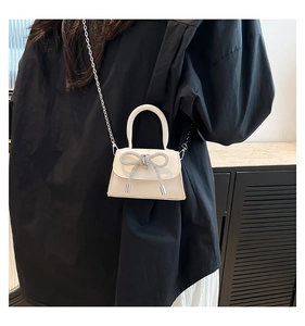 Detail of a cream mini crossbody bag with a sparkling silver rhinestone bow and chain strap