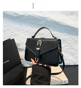 Détail du sac noir motif crocodile avec boucle dorée et poignée sur fond de roche