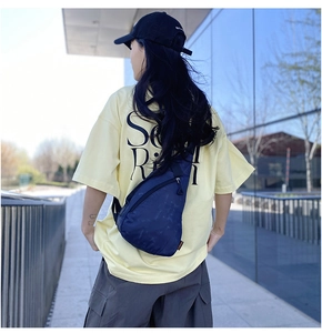 Outdoor street view of a woman wearing a minimalist navy blue nylon crossbody sling bag