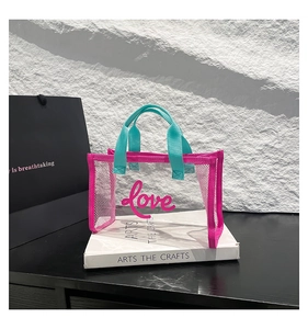 Close-up of clear mesh tote bag with pink love print and blue handles on white books