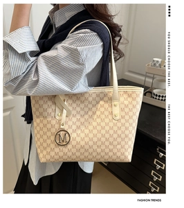 Detail view of beige monogram tote bag with metallic logo charm on a shoulder strap