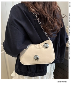 Detail of cream crescent bag featuring silver metallic studs and chain strap on shoulder