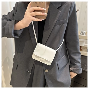 Close-up of white mini square crossbody bag on a grey blazer showing leather texture