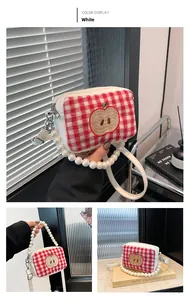 Detail of white crossbody bag with red plaid fabric, apple embroidery and pearl handle
