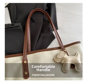 Detail of minimalist tote bag with reinforced brown handles and dog-shaped charm