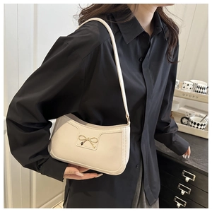 Detail of cream crescent shoulder bag with golden bow clasp on a black shirt background