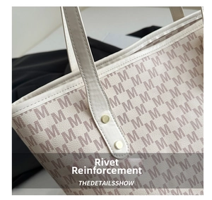 Detail of ivory tote bag featuring M-letter monogram pattern and golden rivets