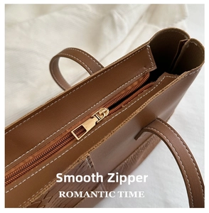 Close-up of golden metal zipper and smooth stitching on a brown faux leather tote bag