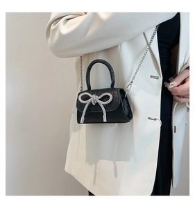 Close-up of black glitter mini bag with rhinestone bow and silver chain strap on model