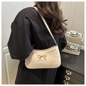 Detail of a beige underarm bag featuring a metallic gold bow buckle and stitching