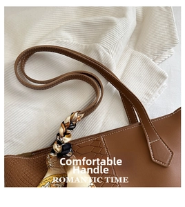 Detail of a brown tote bag handle featuring crocodile texture and a colorful silk scarf