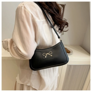Detail of a black leather underarm bag featuring a delicate gold bow metal hardware