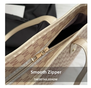 Detail of smooth golden metal zipper and textured logo print on beige leather tote bag