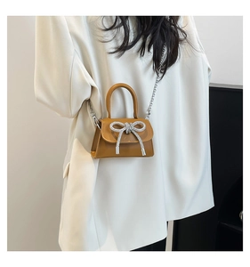 Detail of a brown trapezoid mini bag featuring a large silver rhinestone bow and chain strap