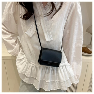 Girl's matte black mini square crossbody bag shown on a white lace outfit in a cozy room