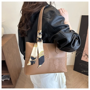 Detailed close-up of brown tote bag with snakeskin texture and decorative silk scarf handle