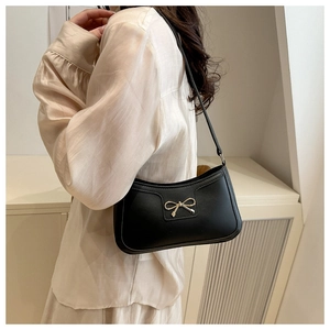 Detail of black leather underarm bag featuring a gold bow accent on a female model
