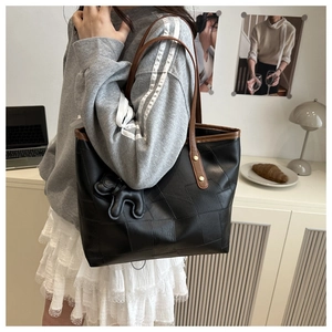 Detail of black leather tote bag with brown handles and a cute plush animal pendant