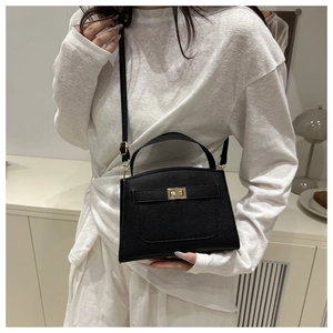 Détail du sac à main noir grainé avec fermoir doré porté sur une tenue blanche