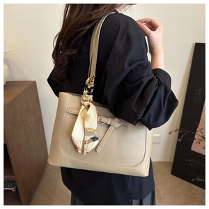 Gros plan d'un sac cabas beige avec foulard décoratif porté à l'épaule par un mannequin