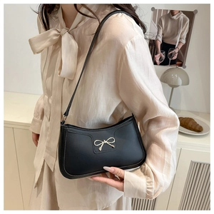 Detail of a black leather underarm bag featuring a gold metal bow buckle and slim strap
